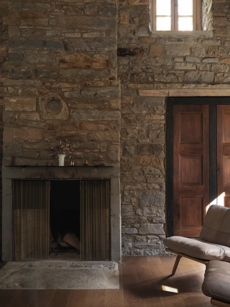 Fireplace with ribbed metal surround set into stone wall next to timber doors in afternoon light
