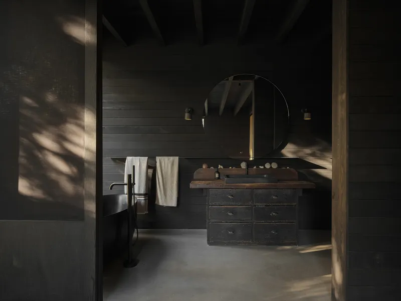 Bathroom with black horizontal plank walls and timber vanity under dappled sunlight