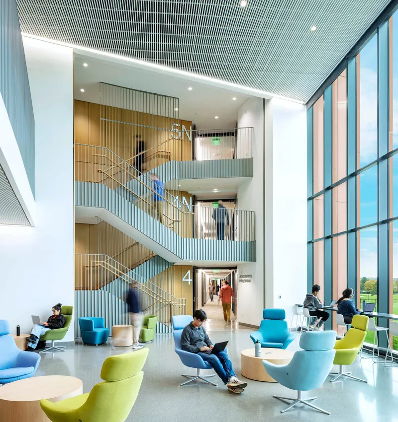 Four-story stairwell with vertical slatted walls, students on seating below, and tall glazing to one side