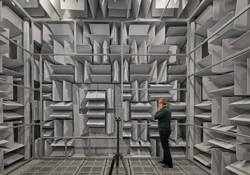 Acoustic testing chamber lined with pyramidal foam baffles and a technician adjusting equipment inside
