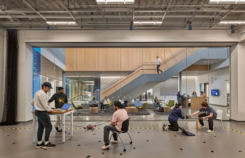 View through glass wall into double-height atrium with staircase and students working with drones