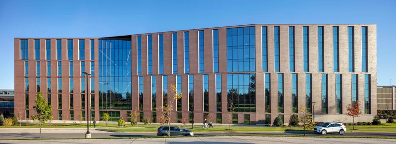 Street view of the striped brick and glass facade under a clear blue sky with young trees