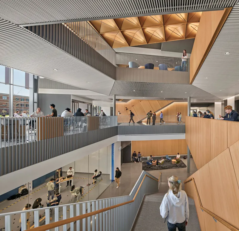 Multi-level atrium with interconnected walkways, triangulated wood ceiling, and students gathering on multiple floors