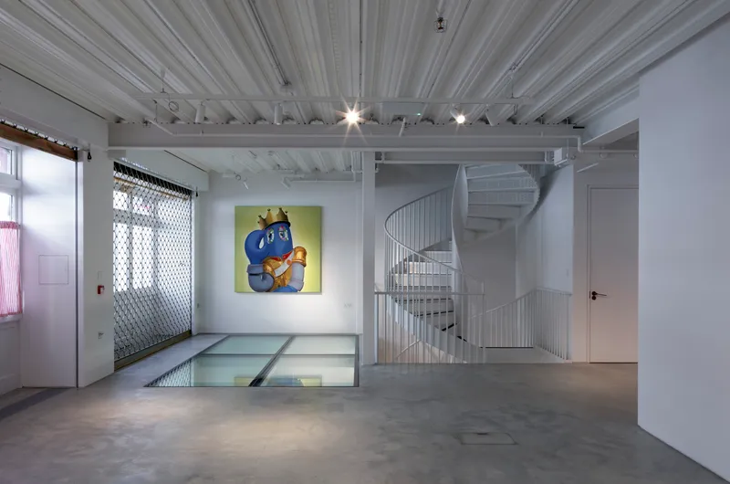White spiral staircase behind mesh railing next to floor opening with glazed panels and pendant lights