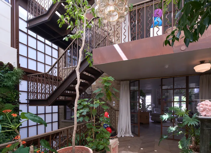 Multi-level interior courtyard with cantilevered balcony, metal wave-pattern railing, and planted trees beneath translucent glass block walls