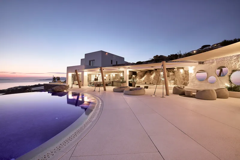 Infinity pool terrace with timber pergola and stone retaining wall at dusk overlooking the sea