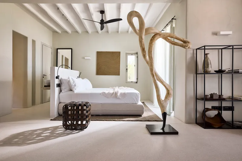 Bedroom with exposed white timber ceiling beams and driftwood sculpture illuminated by afternoon sunlight