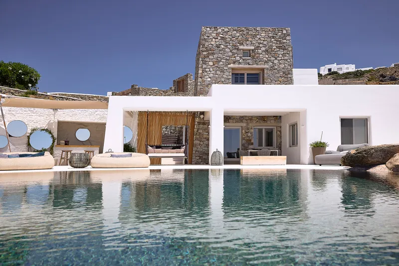Pool deck with circular porthole screens in white pergola facing stone tower volume under clear sky