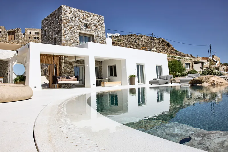 Poolside terrace with curved mosaic edge stepping into water beside white colonnade and stone tower volume