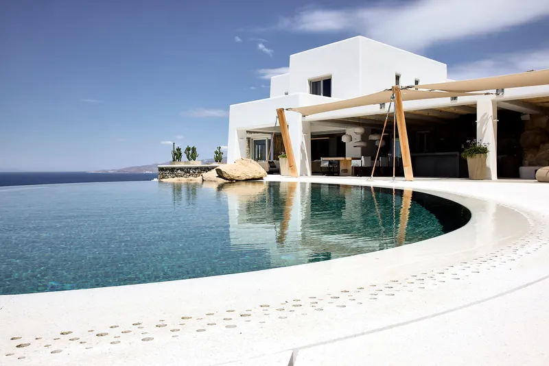 Infinity pool edge with timber pergola columns reflected in still water
