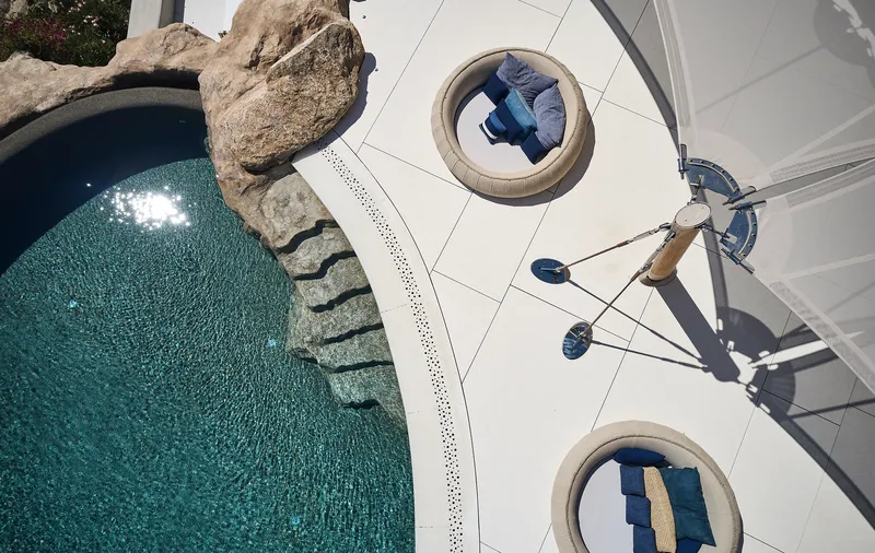 Overhead view of white terrace with circular recessed lounges and person walking beside the pool edge