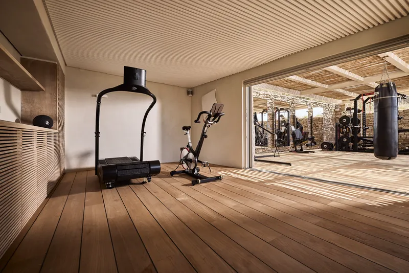 Interior fitness room with slatted timber ceiling and decking opening to an outdoor exercise area with stone walls