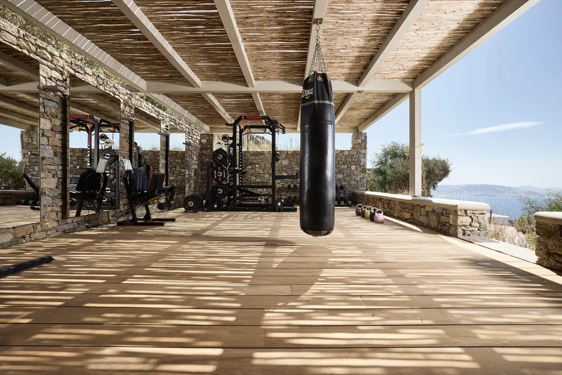 Covered outdoor gym pavilion with exposed timber beams and hanging punching bag overlooking distant hillside landscape