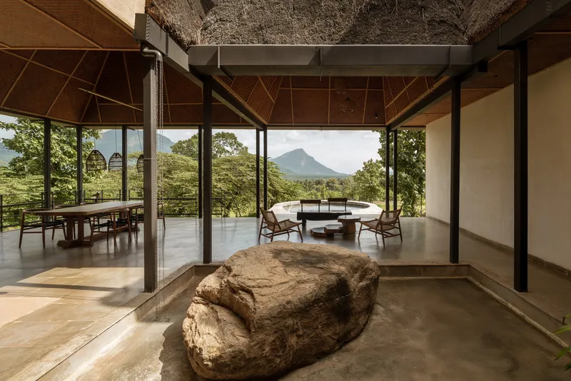 Open interior with polished concrete floor, exposed steel columns, thatch overhead, and a large weathered boulder at center