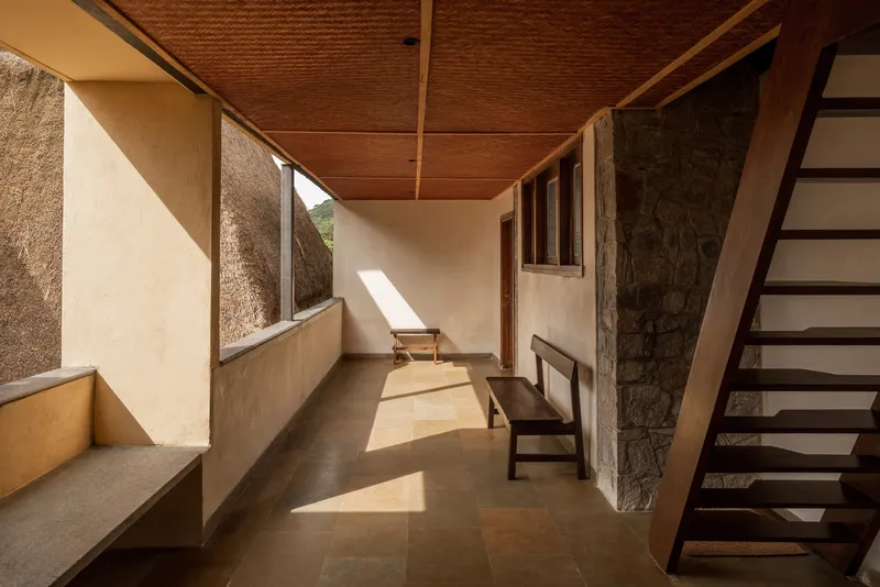 Corridor with woven bamboo ceiling, stone wall, and timber staircase bathed in afternoon sunlight