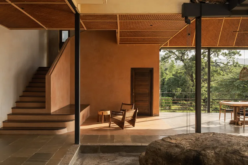 Open living area with woven bamboo ceiling panels, exposed steel beam, and large boulder at floor level