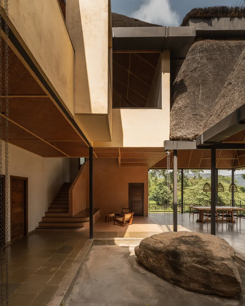 Interior courtyard with timber staircase, large boulder and thatched roof overhang filtering afternoon sunlight