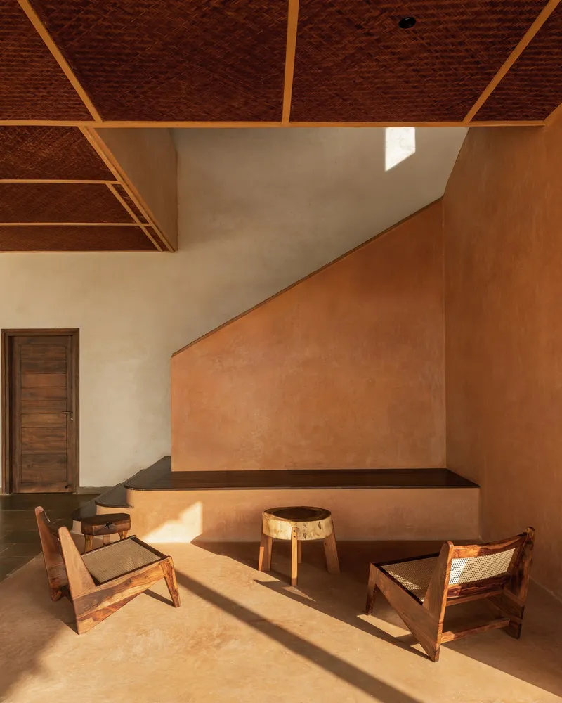 Sunken seating area with ochre plaster walls and thatched ceiling casting afternoon light across stone floor