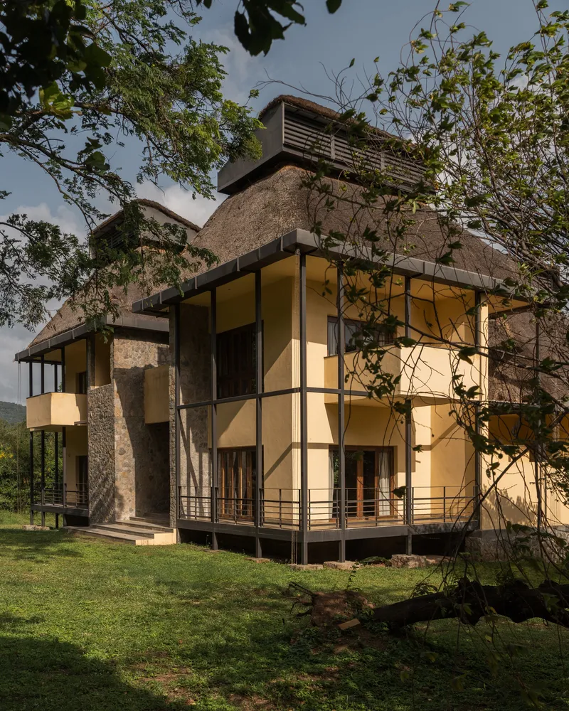 Corner facade showing yellow panels, stone cladding, black steel framing, and a thick thatched roof in afternoon light