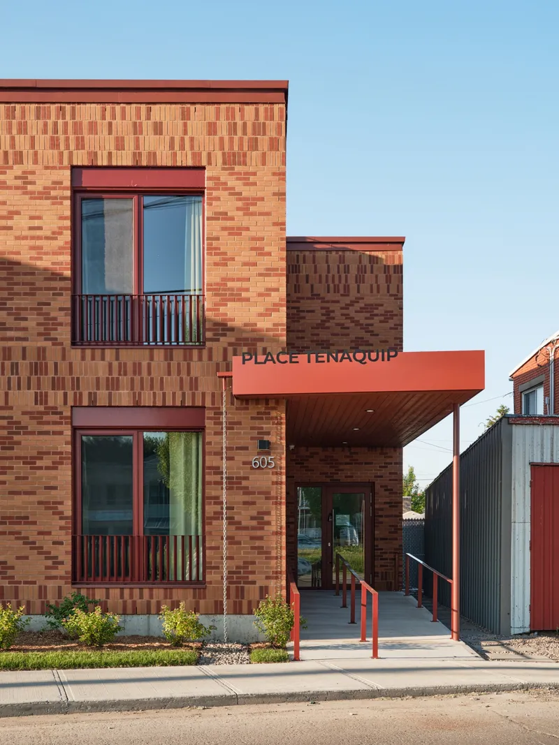 Main entrance with cantilevered red canopy and vertical balcony railings under afternoon light