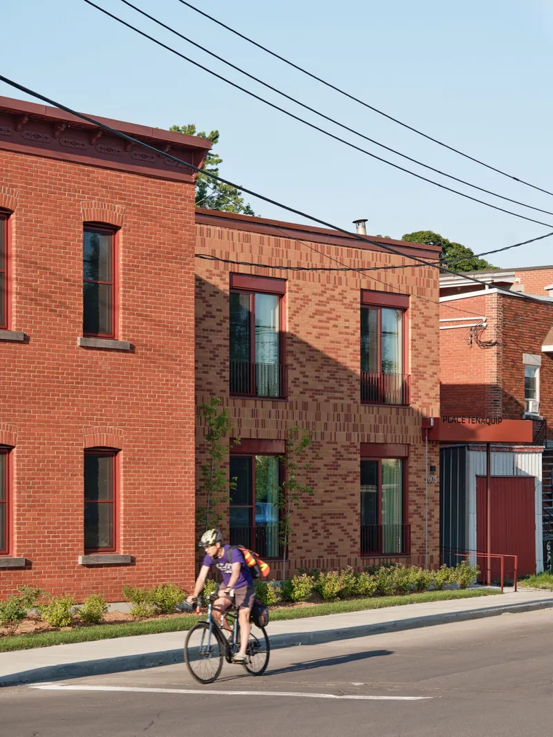 Street view of the brick facade with a cyclist passing the planted edge at ground level