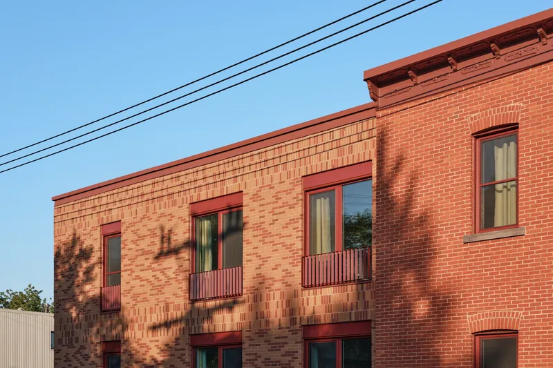 Upper facade showing textured brick volumes with balconies beneath diagonal power lines at dusk
