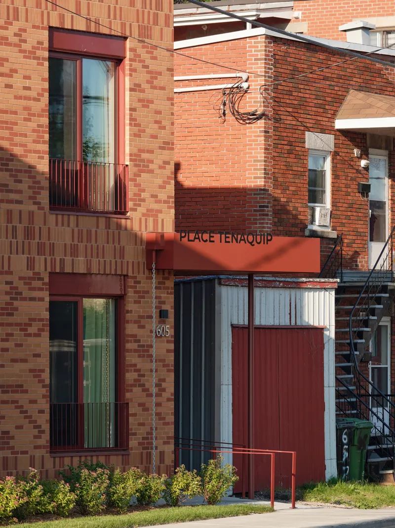 Street view of the multicolored brick facade with projecting windows and red canopy in afternoon light