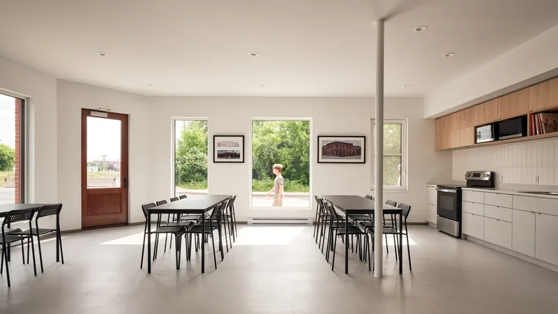Communal dining room with large picture windows framing green foliage and a figure passing outside