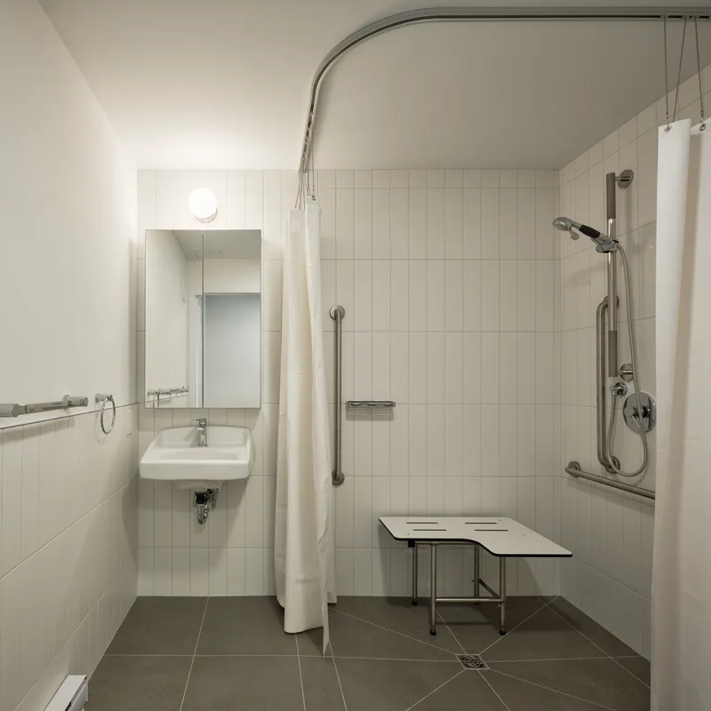 Accessible bathroom with wall-mounted sink, curved curtain rail, grab bars, and fold-down shower bench