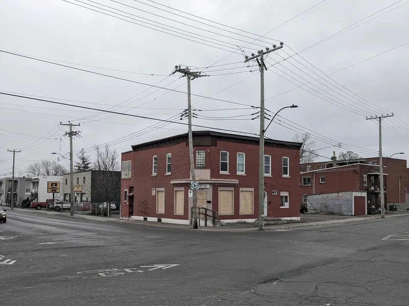 Corner view of existing brick building with boarded windows beneath power lines on an overcast day