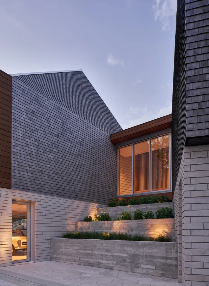 Courtyard view of textured concrete planter walls with lighting beneath planted beds at dusk