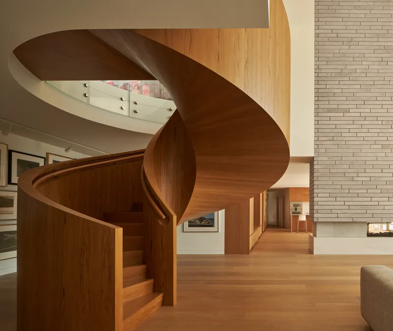 Freestanding helical timber staircase beside the brick wall in the double-height living space