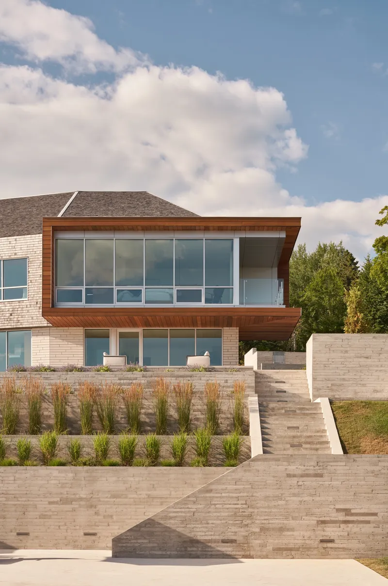 Tiered stone retaining walls with planted beds below the two-story facade in afternoon light