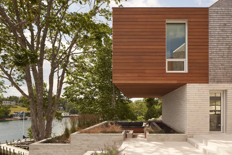 Cantilevered wood-clad box above a limestone base and waterside planting beds with lake beyond