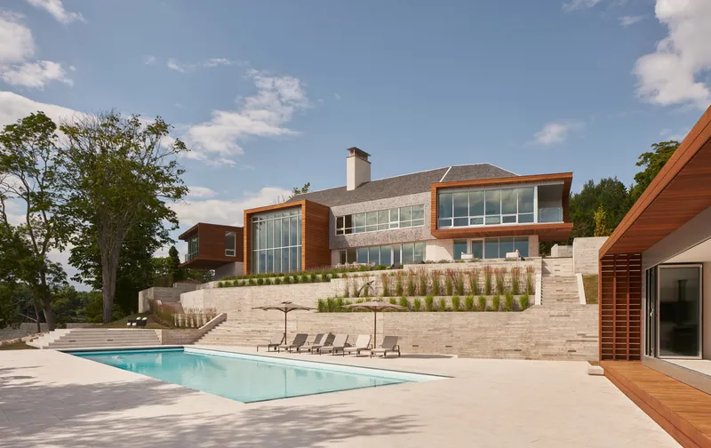 Rear view of the residence with tiered limestone retaining walls and rectangular pool under afternoon sun