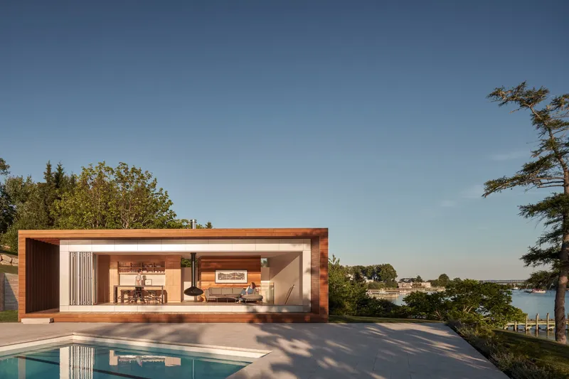 Timber-clad poolside pavilion with open living space overlooking the water at golden hour