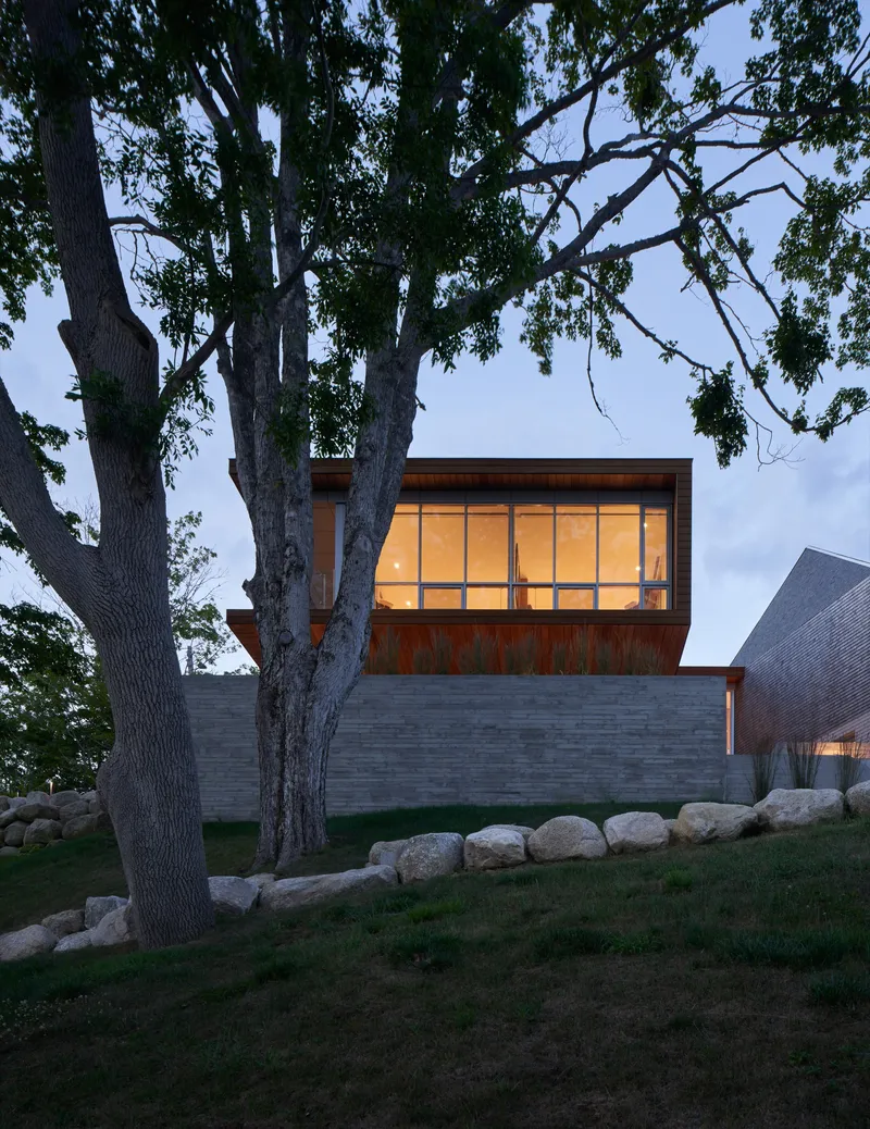 Cantilevered timber and glass upper volume above horizontal brick base with stone retaining wall