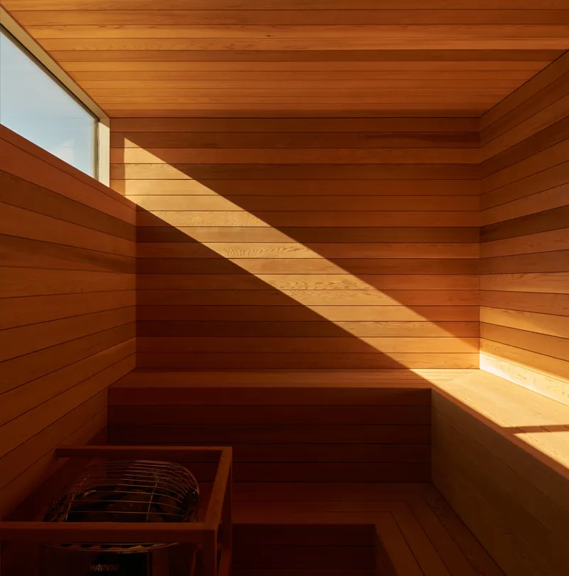 Cedar-lined sauna interior with tiered benches and diagonal sunlight through clerestory window