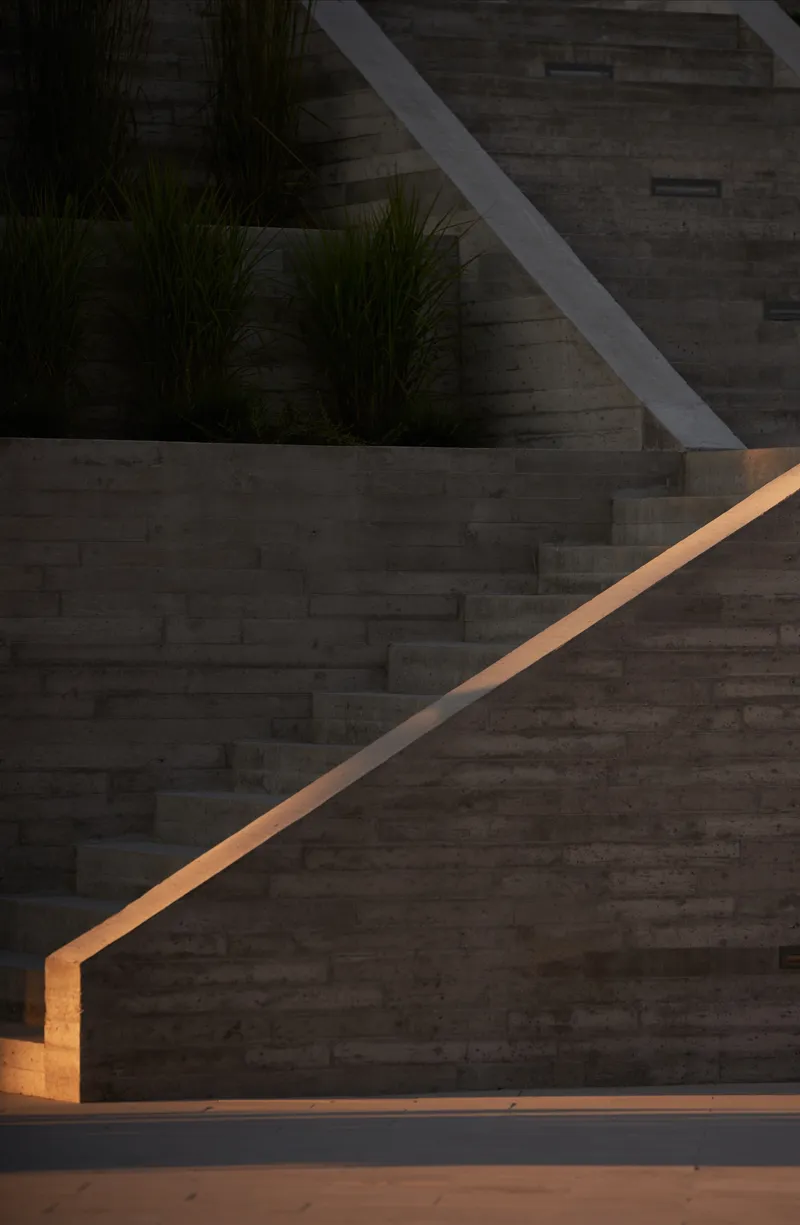 Exterior concrete stair with illuminated bronze handrail ascending at dusk