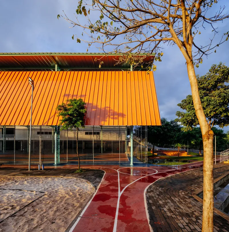 Orange corrugated facade with mesh screens below and a leafless tree in the foreground at dusk