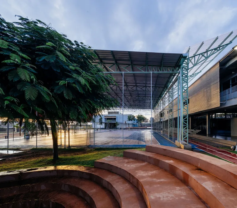 Curved amphitheater steps in red concrete leading to the courtyard with tropical trees beside them