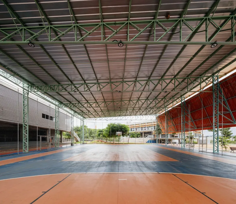 Open-air court under metal deck roof with green tubular columns and orange wall on right