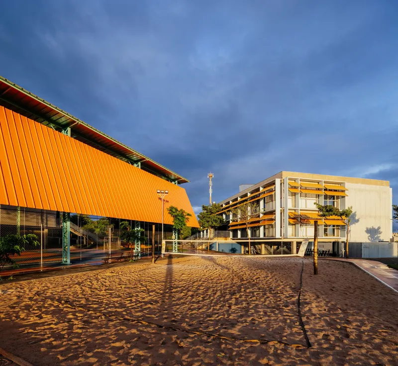 Courtyard view showing orange canopy gymnasium and pale concrete classroom block under dark sky