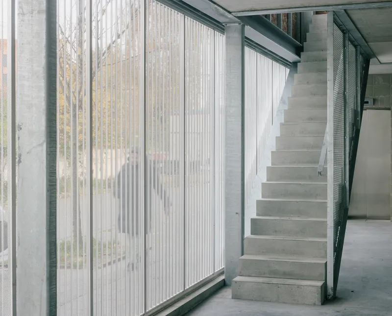 Concrete staircase rising alongside fluted glass panels with a view to the exterior garden