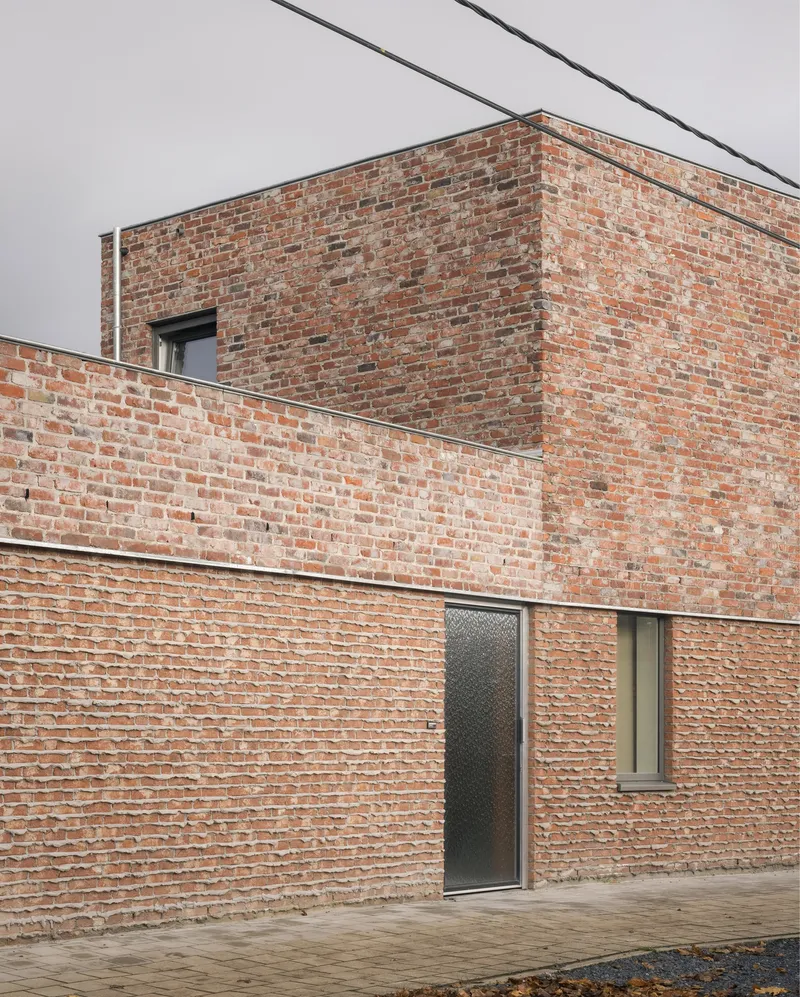 Brick facade volumes with recessed openings and overhead power lines against a pale sky