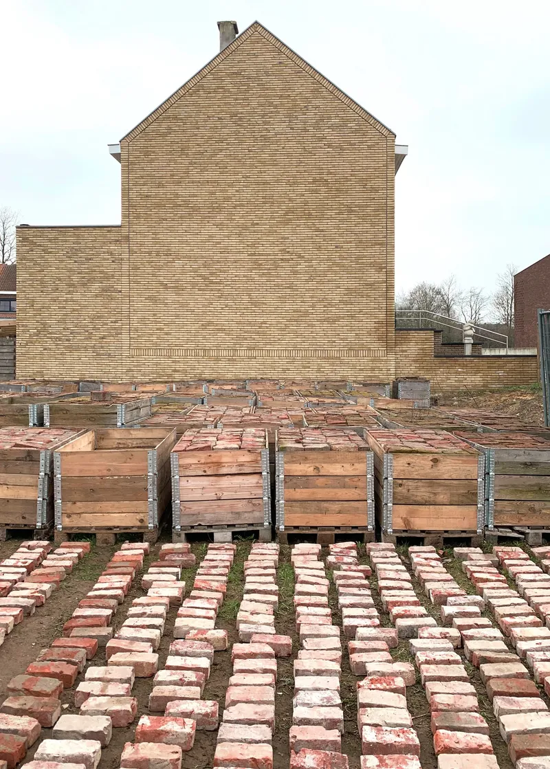 Courtyard with timber formwork planters and rows of laid bricks fronting a brick gable wall