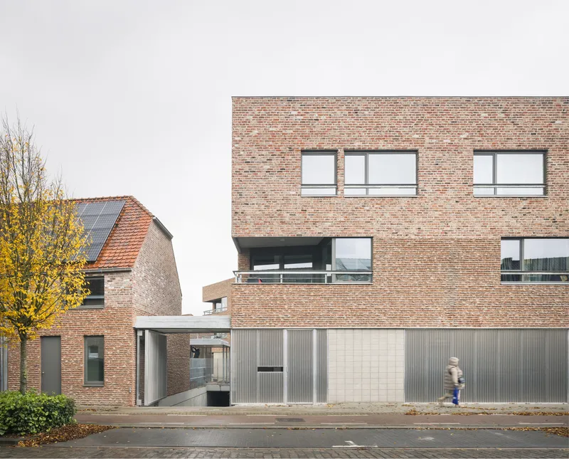 Street view of brick facade with corrugated metal base and a pedestrian passing in autumn