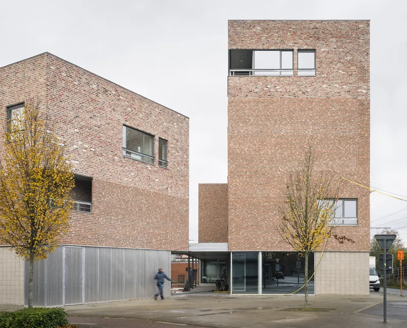 Stacked brick volumes with corrugated base and young trees in a paved courtyard