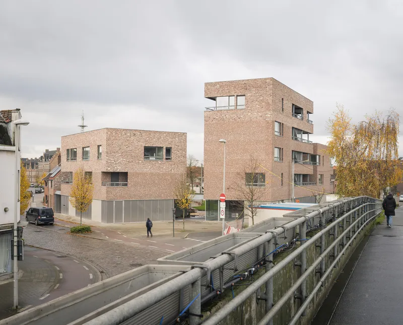 View from bridge showing brick housing blocks with ground-level glazing under overcast sky