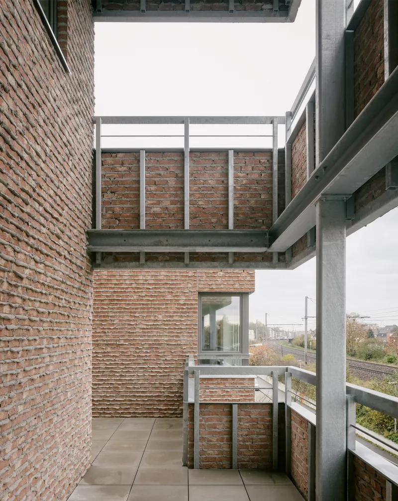 Concrete balcony framed by brick walls with metal railings overlooking rail tracks